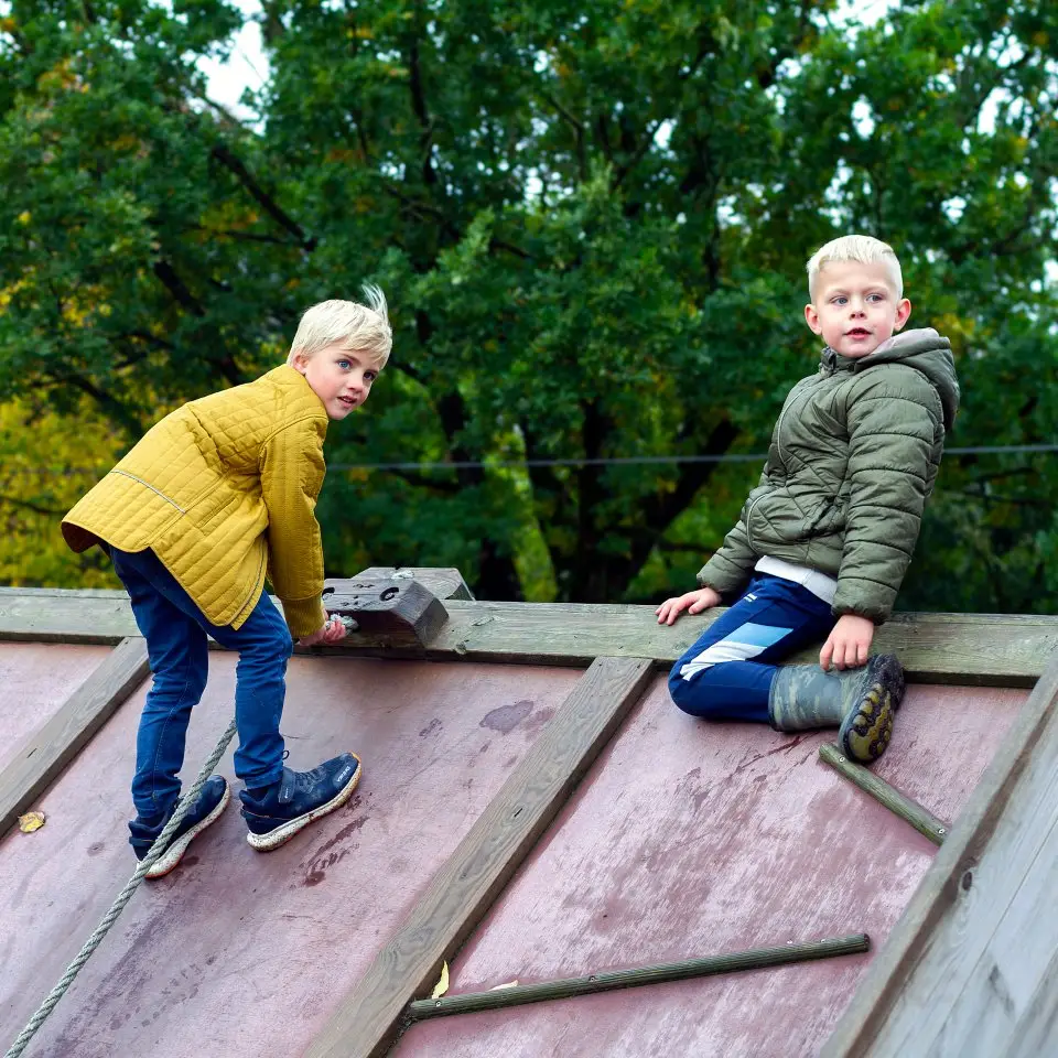 To drenge klatrer på et legehus af træ